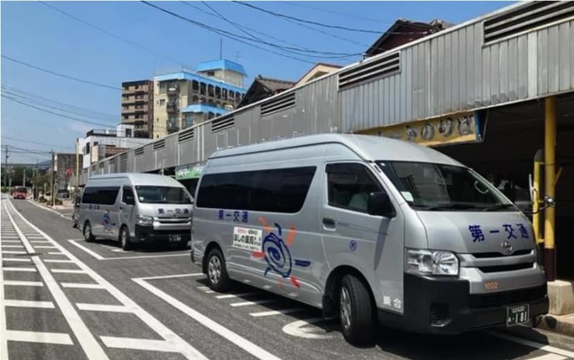 銀色の小型バスのような乗合タクシーが、商店の並ぶ道路に2台停まっている写真。車体の側面に第一交通の文字とマークがある