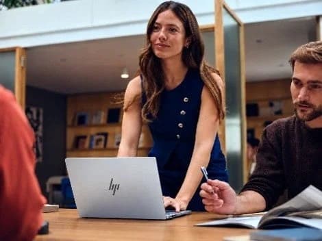 会議室のテーブルでHPのノートPCを開き、立って話す女性と、資料を見る男性