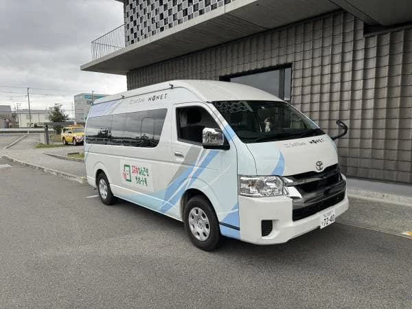 白い小型のバンの車両。側面に「スマホなんでもサポート号」と読める表示があり、建物の前の駐車場に止まっている